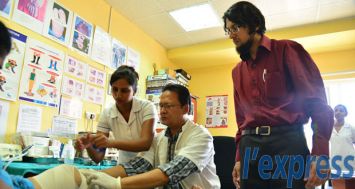 Swaley Maherally (assis) et le Dr Yaasir Ozeer (à dr.), diabétologue au Diabetes Vascular Health Centre de Souillac, inspectant le pied d'un patient souffrant de diabète.© Beekash Roopun 