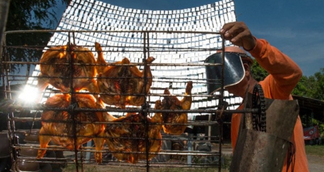 Sila Sutharat, 60 ans s'installe le poulet dans une grille et positionne l'assemblage de miroirs pour que la réflexion du soleil soit parfaite.