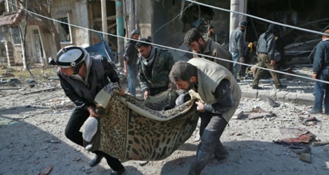 Du personnel de la Défense civile, connu sous le nom de Casques blancs, transporte un corps après un bombardement attribué au régime syrien sur une localité rebelle de la Ghouta orientale, le 27 novembre 2017 