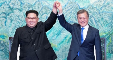 Le président sud-coréen Moon Jae-in (d) et le leader nord-coréen Kim Jong Un lèvent leurs mains unies pendant le sommet intercoréen, le 27 avril 2018 à Panmunjom.