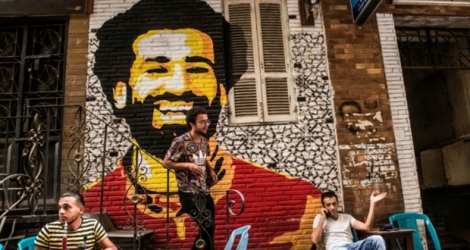 Ahmed Fathy (c), un artiste égyptien, joue devant une peinture murale du joueur de Liverpool, Mohamed Salah, dans un café de plein air au Caire, le 30 avril 2018.