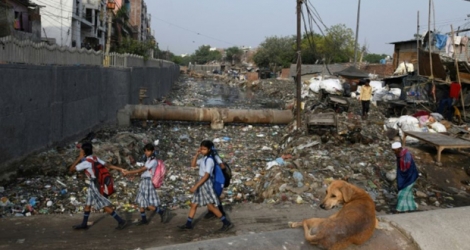 Des écolières passent devant un canal d'évacuation des égoûts rempli de déchets dans le bidonville Taimur Nagar à New Delhi le 30 mai 2018