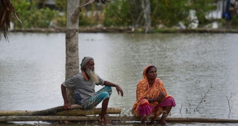Un couple assis sur un tronc d'arbre près de leur maison encerclée par les eaux à Khulna (Bangladesh), le 4 mai 2019, après l'arrivée du cyclone Fani, dont l'intensité a fortement faibli.