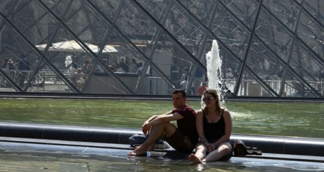 Des touristes se rafraîchissent dans un bassin devant la Pyramide du Louvre le 26 juin 2019.