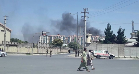 Des passants dans une rue de Kaboul devant un panache de fumée qui s'élève depuis le site d'une attaque, le 1er juillet 2019.