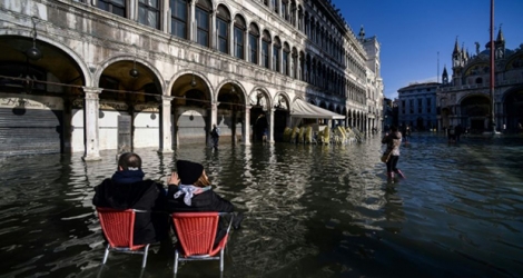 Un couple assis sur des chaises de café observe la place Saint-Marc inondée, à Venise le 14 novembre 2019.