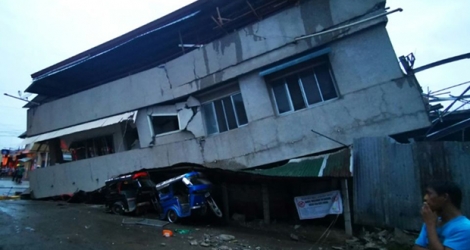 Des habitants observent une maison détruite avec un véhicule coincé dessous après un puissant séisme, à Padada dans la province de Davao del Sur sur l'île de Mindanao aux Philippines le 15 décembre 2019.