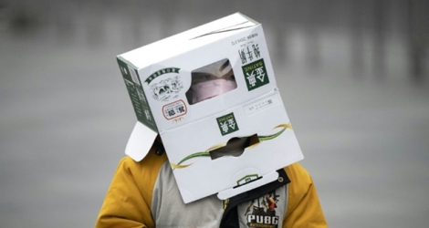 Un jeune garçon porte un carton sur sa tête, en plus d'un masque de protection, à la gare ferroviaire de Shanghai, le 13 février 2020. 