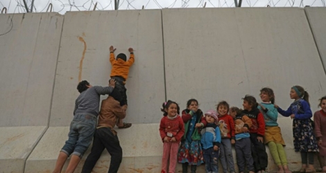 Des enfants déplacés syriens tentent d'escalader le mur de la frontière turque, dans la province d'Idleb, le 21 février 2020.