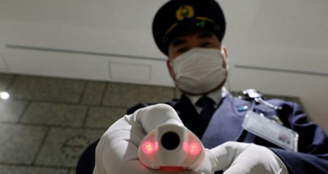 Un agent de sécurité montre un appareil de mesure de la température corporelle, à la réception d'un bâtiment officiel de Tokyo le 5 mars 2020.