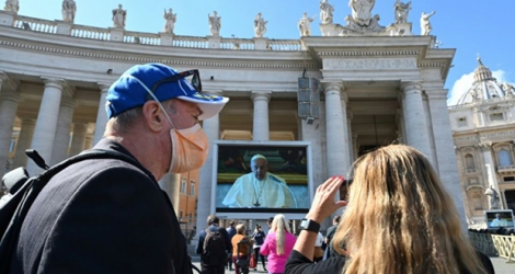 Un couple prend une photo du pape prononçant la prière dominicale depuis sa bibliothèque privée, et retransmise sur des écrans géants sur la plce Saint-Pierre de Rome, le 8 mars 2020, en raison de l'épidémie du nouveau coronavirus.