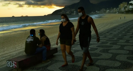 Des promeneurs portent des masques pour limiter la propagation du nouveau coronavirus, sur la célèbre plage d'Ipanema à Rio de Janeiro, le 19 mai 2020 (AFP)