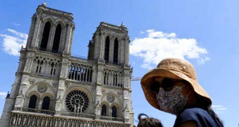 Une femme portant masque et chapeau se tient devant la cathédrale de Notre-Dame qui a rouvert au public, le 31 mai 2020.