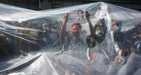 Photo prise le 9 février 2021 montrant des manifestants en Birmanie sous un plastique les protégeant des canons à eau de la police à Rangoun. afp.com - STR