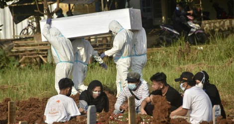 Une famille se recueille sur la tombe d'un proche décédé du Covid-19 pendant que des employés du cimetière se préparent à enterrer une autre victime du virus, le 2 juillet 2021 à Bekasi, en Indonésie.