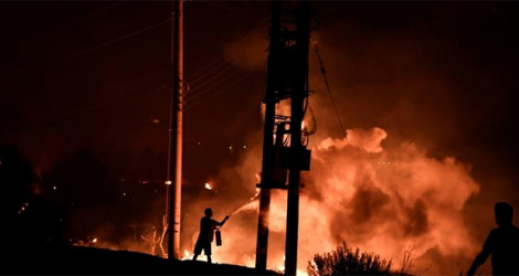 Un homme tente de lutter contre le feu avec un extincteur, le 3 août 2021 à Dekelia, au nord d'Athènes.