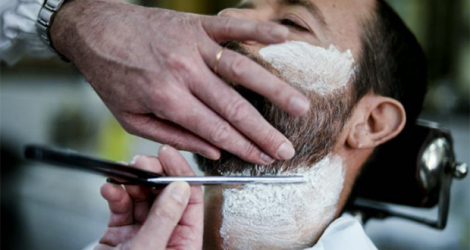Un homme se fait tailler la barbe chez un barbier.