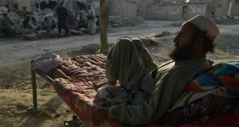 Un habitant allongé sur un lit de camp devant des maisons détruites par un séisme dans la province de Paktika, le 25 juin 2022 en Afghanistan.