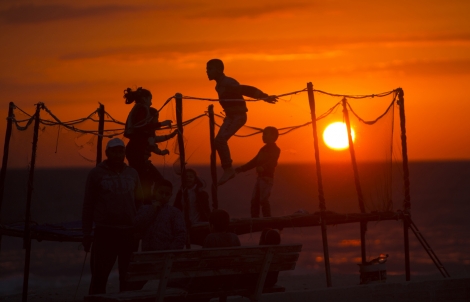 Des enfants palestiniens jouant au trampoline sur la plage de Gaza, au coucher du soleil. 